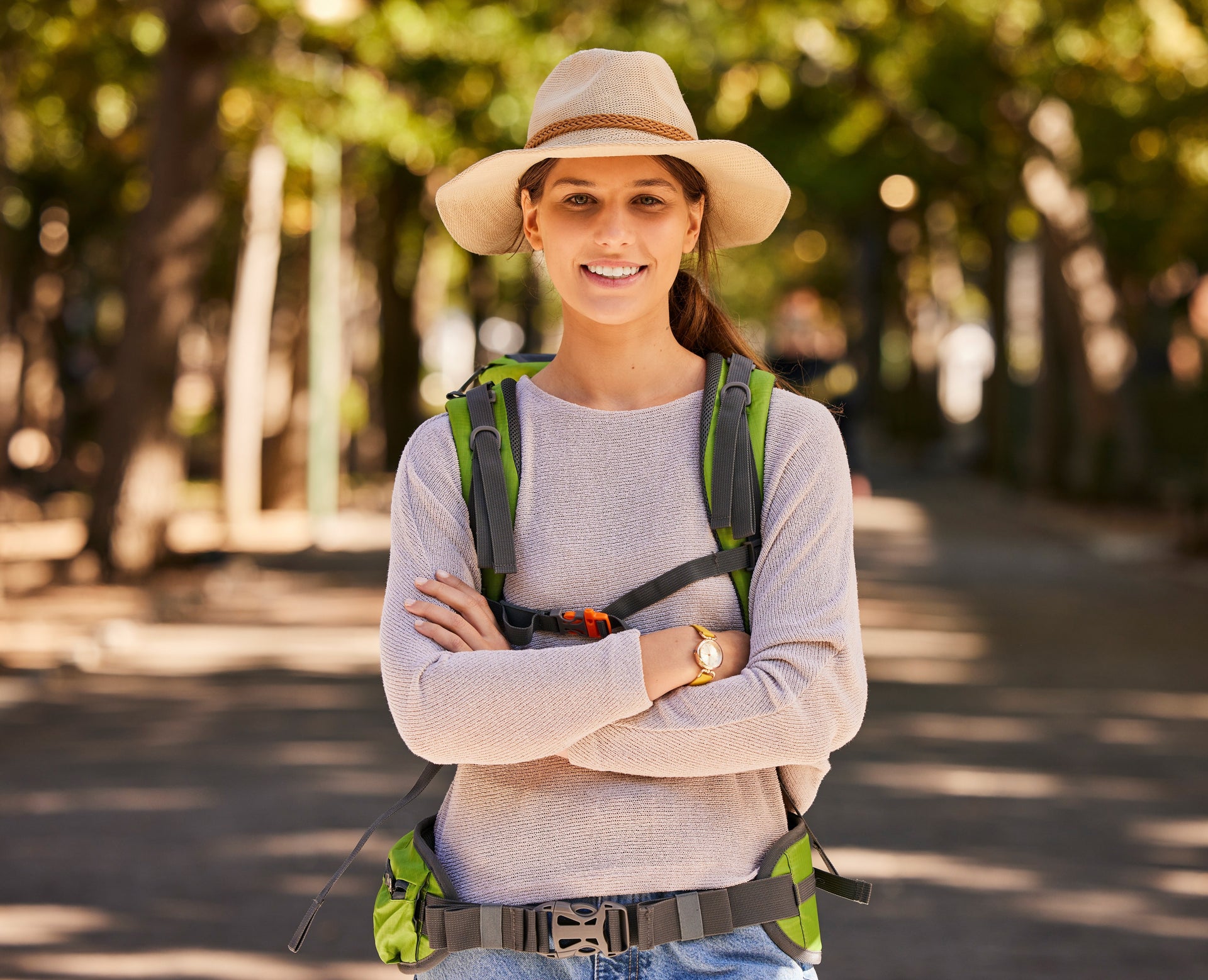 Woman with a backpack and hat standing on a path with trees in the background