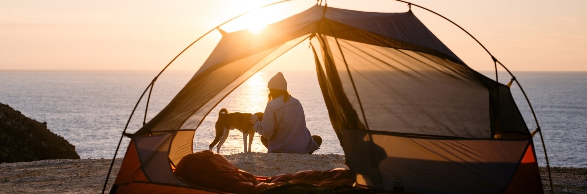Person sitting inside a tent by the ocean at sunset