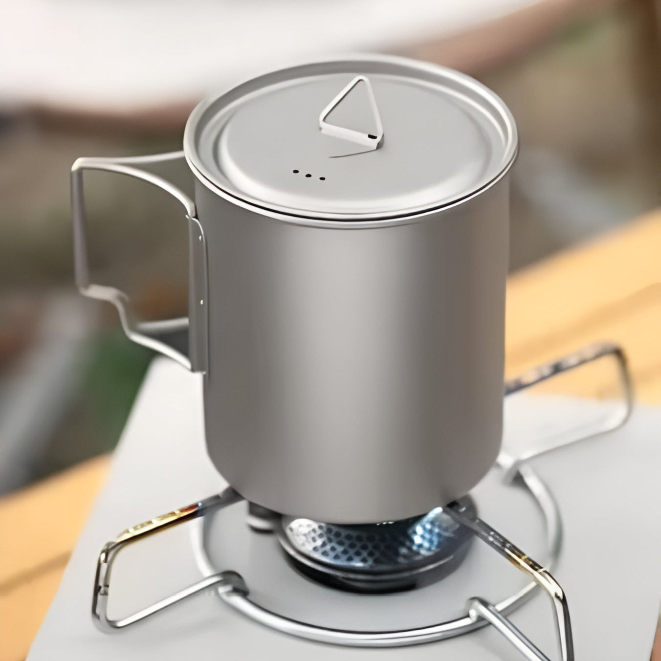 Silver camping mug with a lid on a small stove